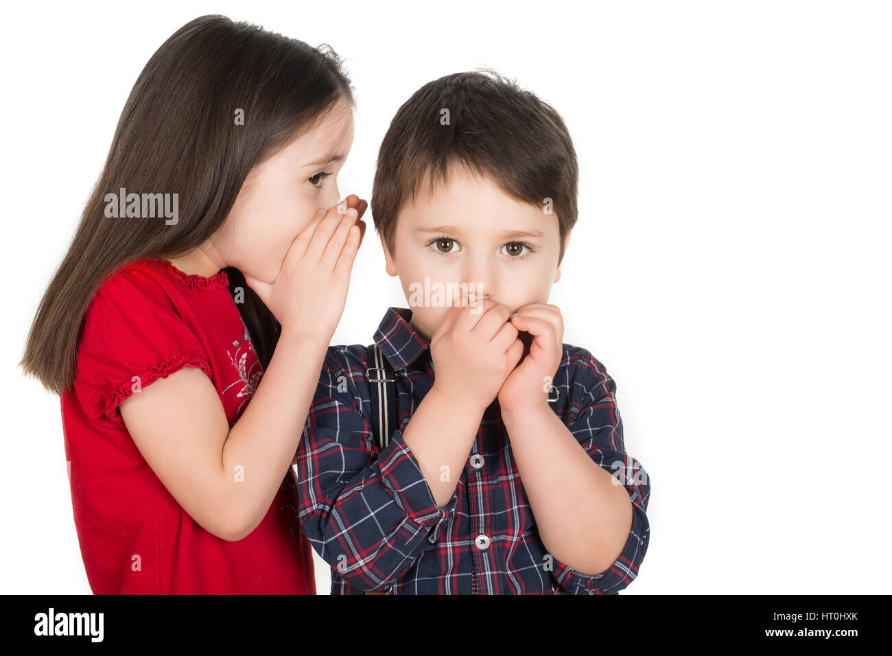 Girl whispering in a little boy`s ear. Boy covering his mouth with his hands. Scared or he cant believe. Isolated on a white background. Stock Photo